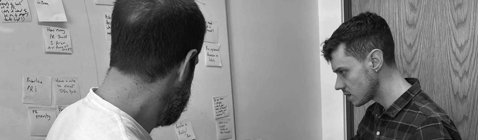 Photo of Chris during a workshop, reviewing post-its on a whiteboard.